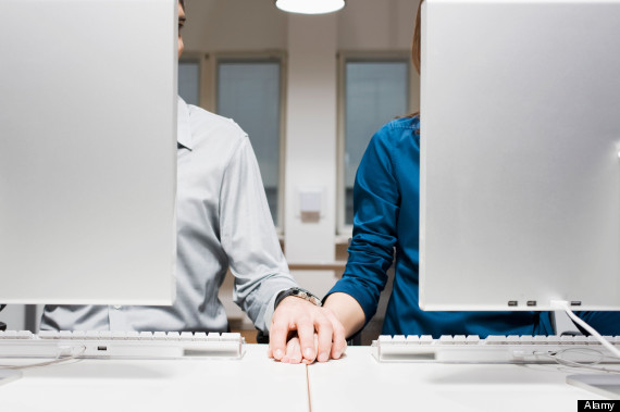 BJ0MKC young couple sitting behind computers in office holding hands